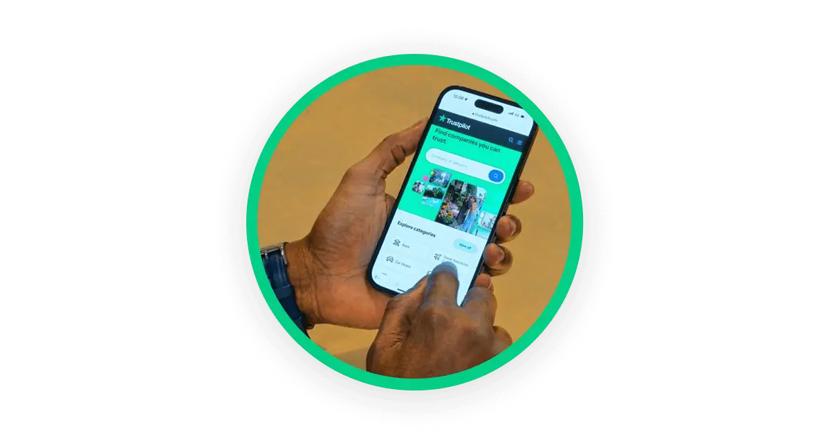 A circular image showing a close up of someone's hand, holding a smartphone that is displaying the Trustpilot website